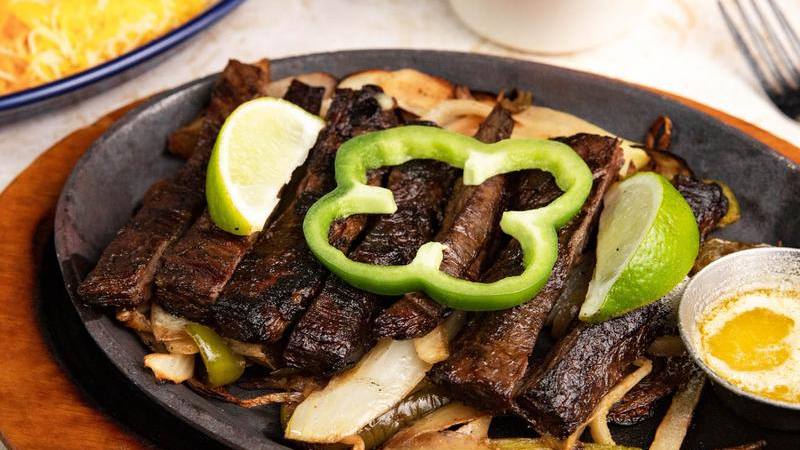 Beef fajitas on the skillet with a green pepper ring and lime