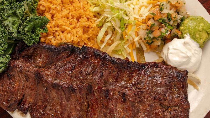 A grilled steak with rice, greens and guacamole