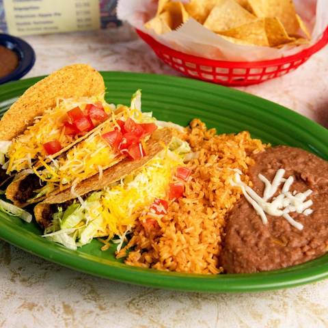 Crispy tacos with lettuce, tomato and cheese on a green plate