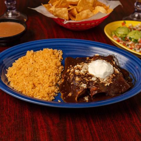 Enchiladas de mole with sour cream and rice on a blue plate