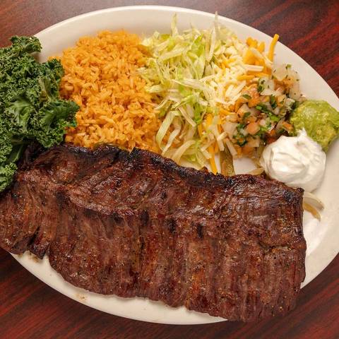 A grilled steak with rice, greens and guacamole