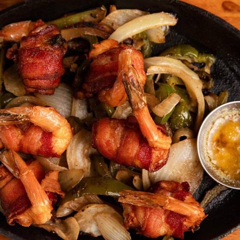 Brochetas: bacon-wrapped shrimp on a sizzling skillet with onions and peppers