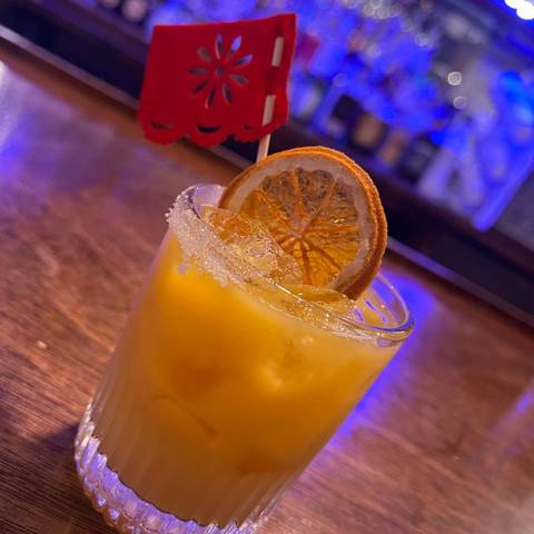 A mango cocktail with a dried orange slice on the bar